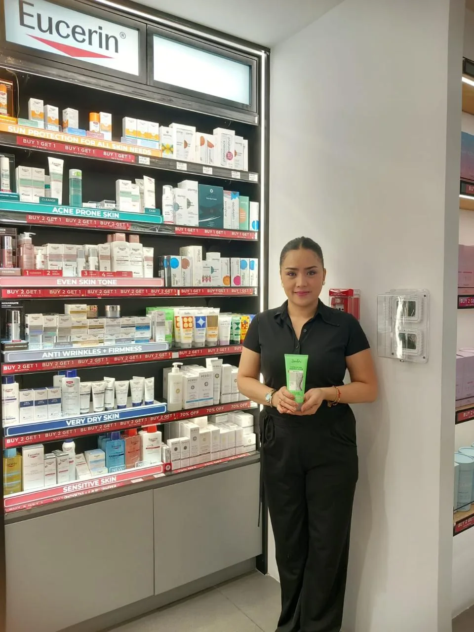 A brand ambassador holding a skincare product in front of a pharmacy dermo-cosmetics shelf.