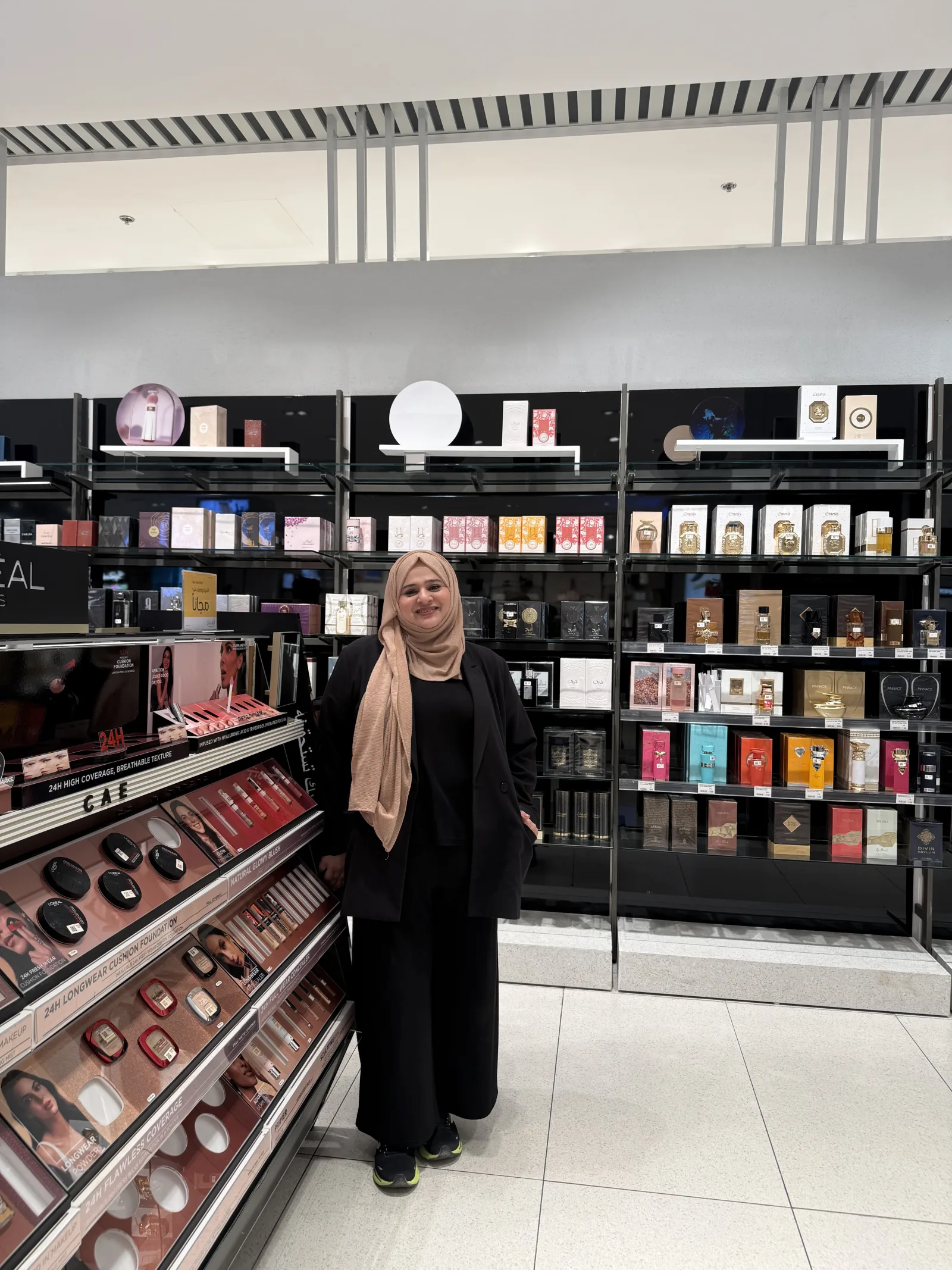 A beauty advisor on the L'Oréal beauty floor, in front of the fragrance and cosmetics wall.
