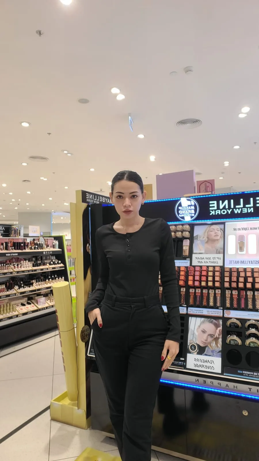 A beauty advisor on the floor of the beauty hall beside the Maybelline New York fixture.