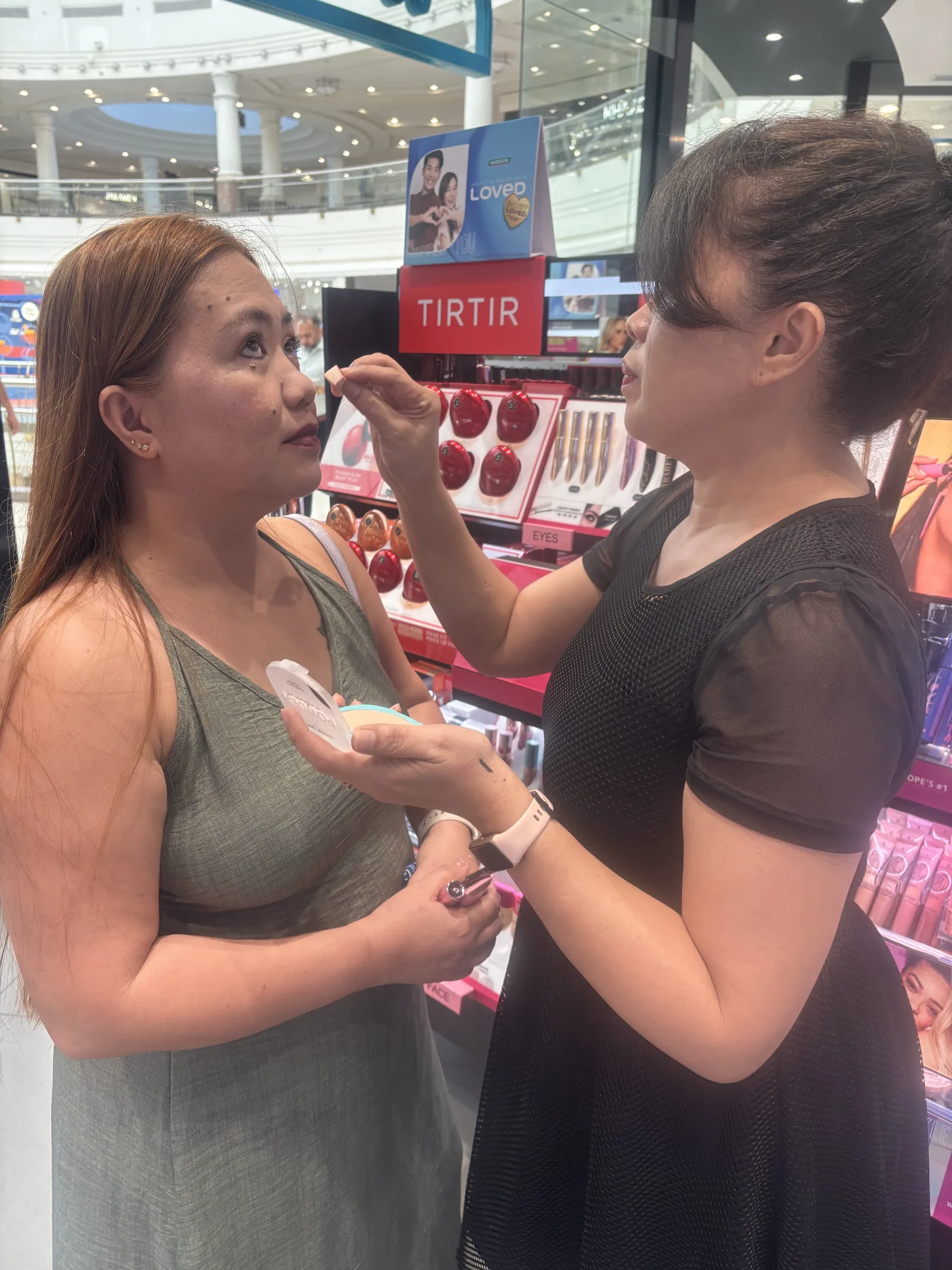 A beauty advisor applying a product for a customer at an in-store beauty counter.