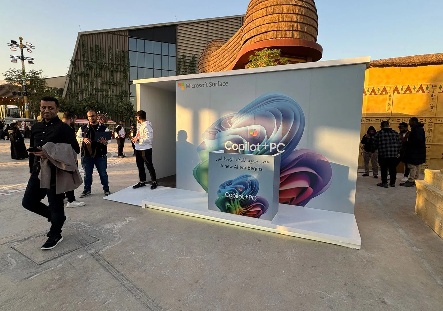 The Copilot+ PC pop-up drawing a crowd at dusk, a branded plinth reading “A new AI era begins” at its centre.