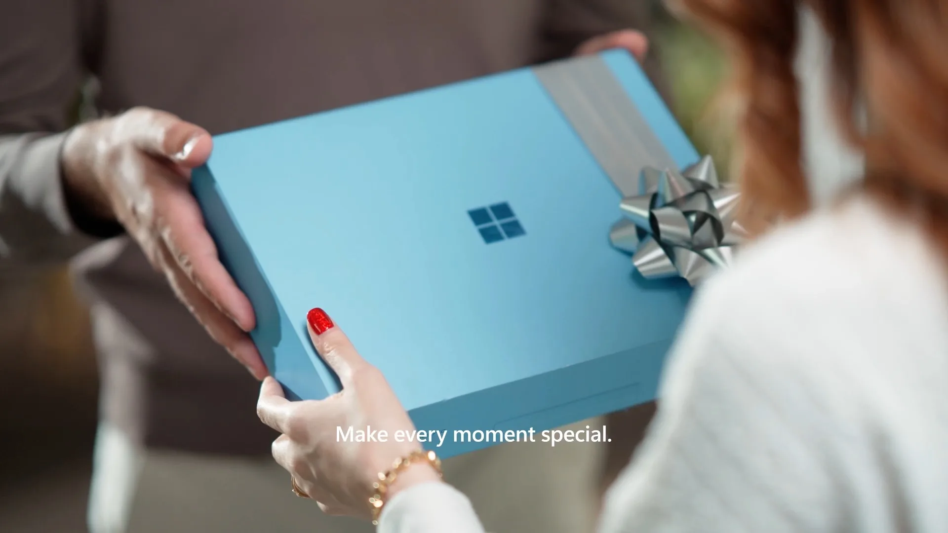 A blue Surface, tied with a silver gift bow, handed from one person to another