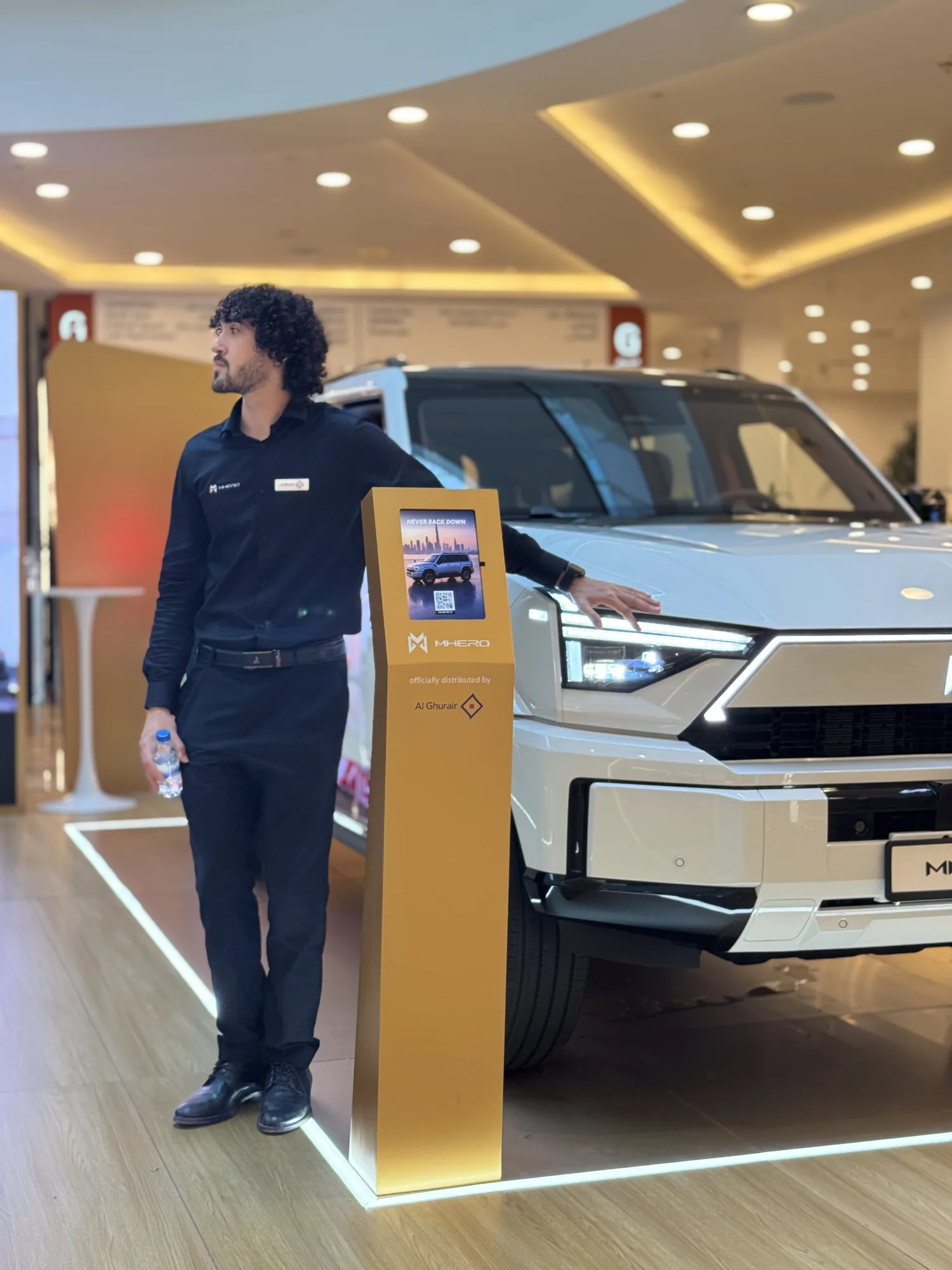 A brand ambassador beside a MHERO information kiosk at the indoor stand.