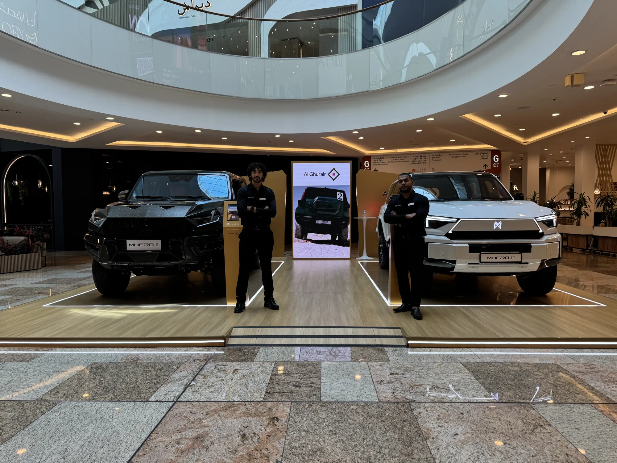 Two Promocell brand ambassadors at the indoor MHERO stand, between the black MHERO I and white MHERO II.