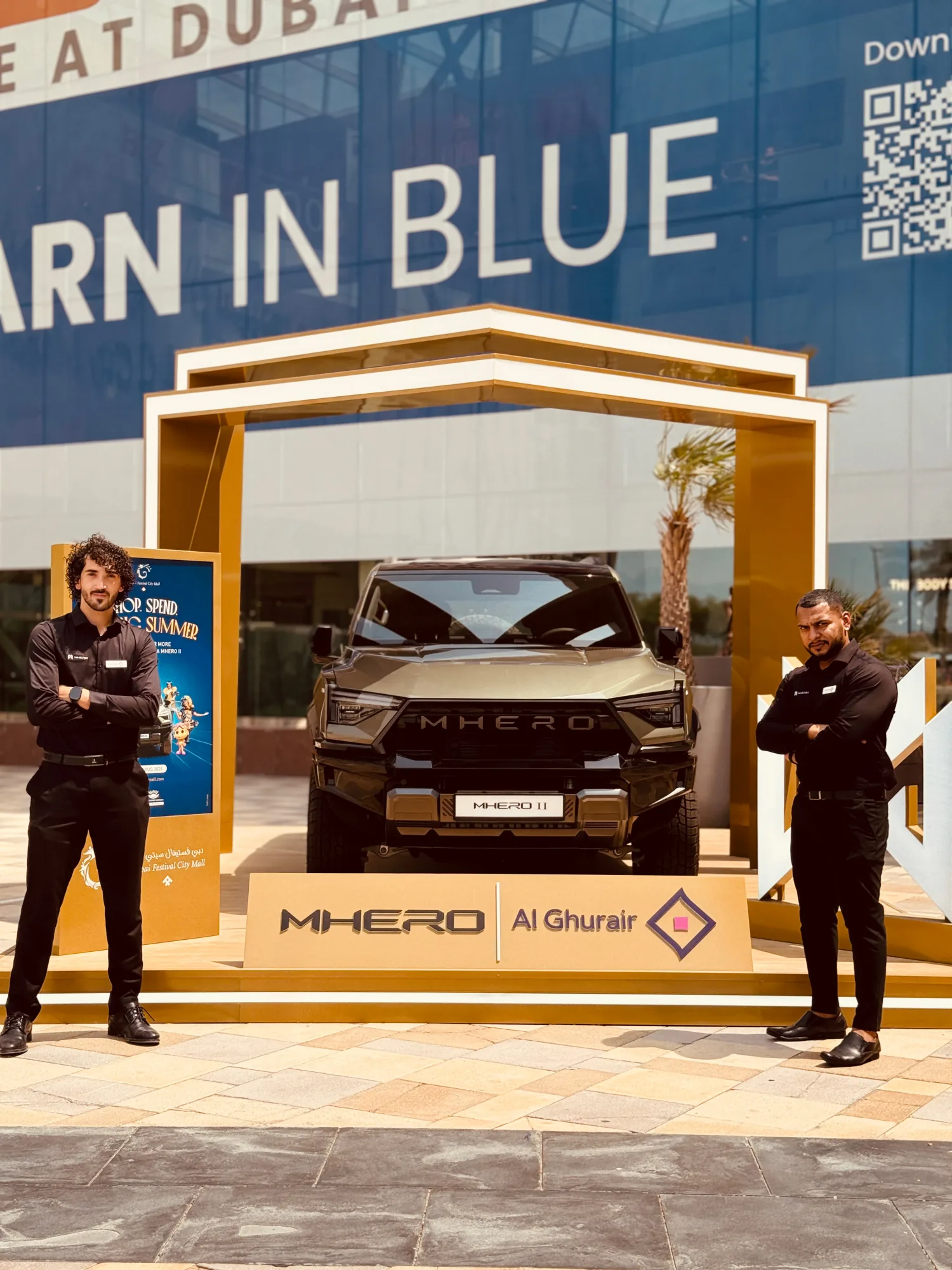 Two ambassadors flanking the MHERO II beneath the outdoor gold gateway stand.