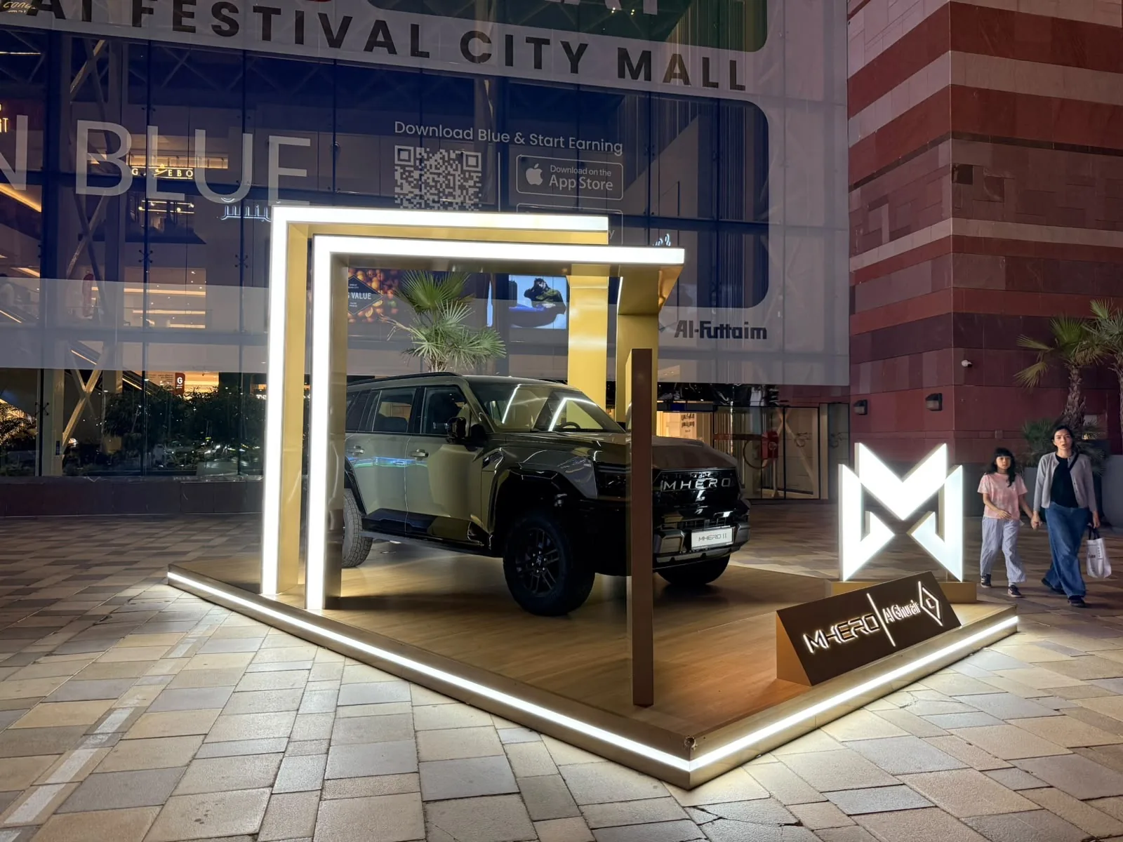 Night view of the outdoor MHERO stand lit up outside Dubai Festival City Mall.