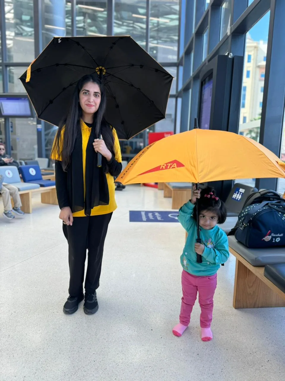 An UmbraCity brand ambassador and a young girl holding bright yellow RTA umbrellas inside a Dubai station.