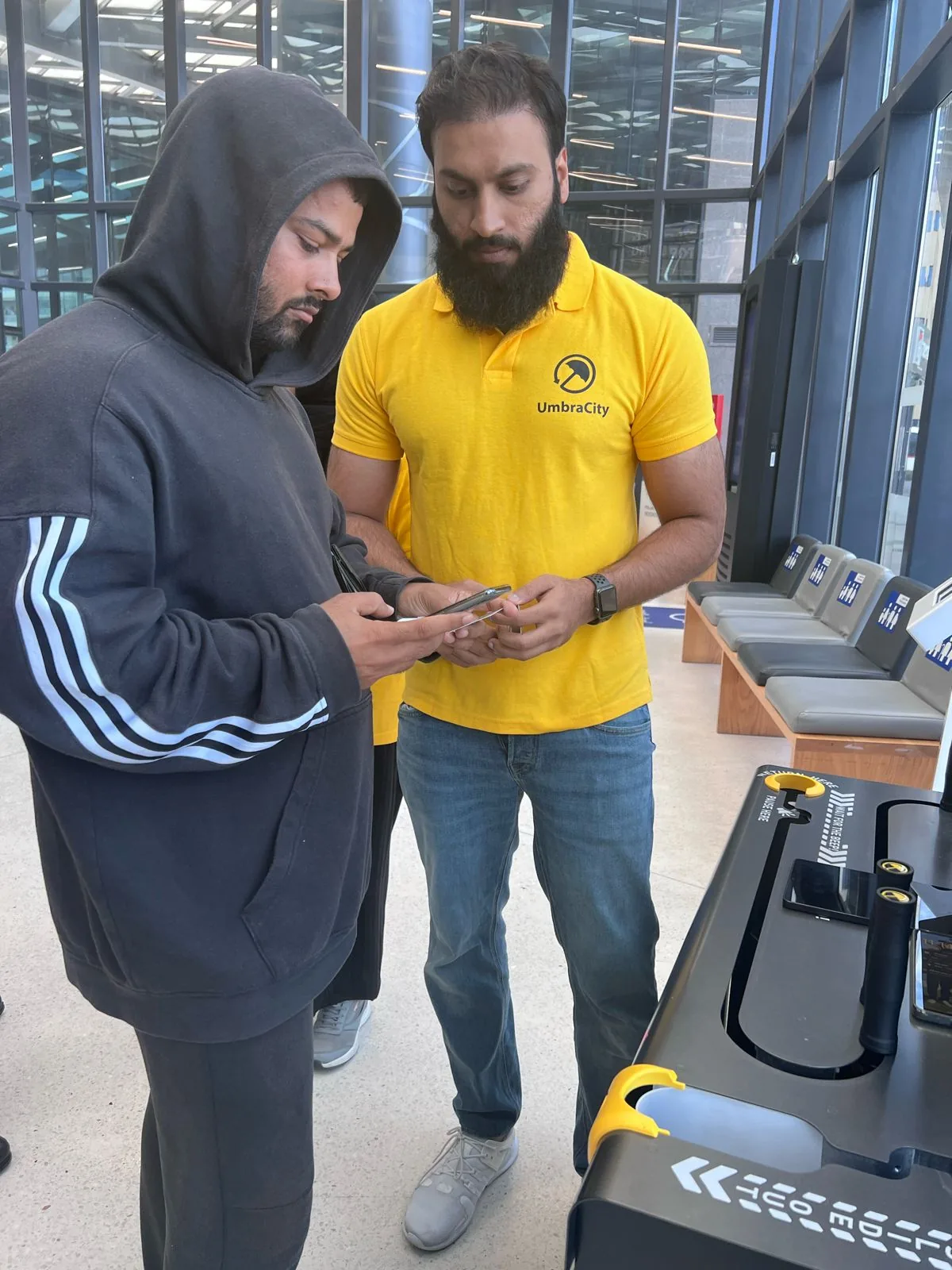 An UmbraCity team member in the yellow uniform helping a commuter borrow an umbrella from the station kiosk.