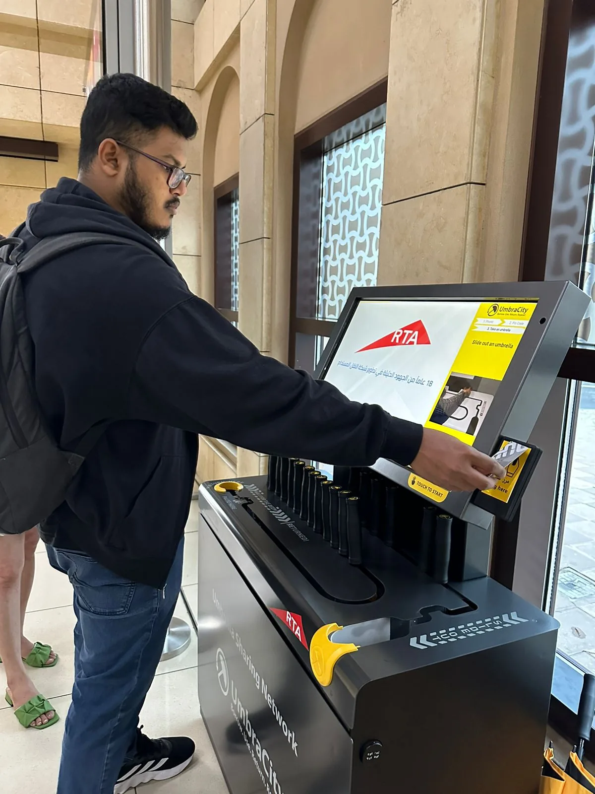 A commuter sliding an umbrella out of the UmbraCity and RTA kiosk at a Dubai Metro station.