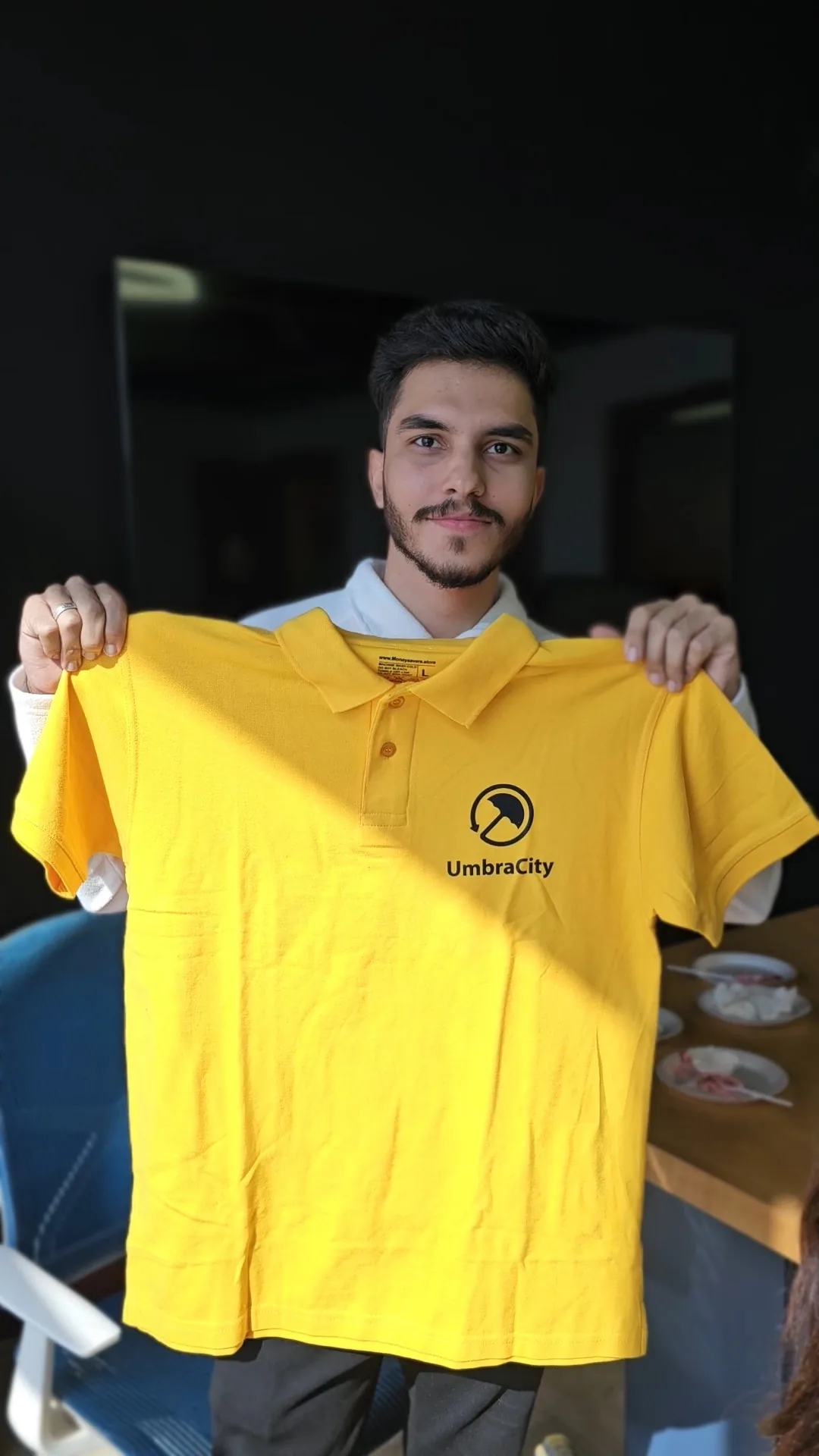 An UmbraCity team member holding up the bright yellow UmbraCity uniform polo.